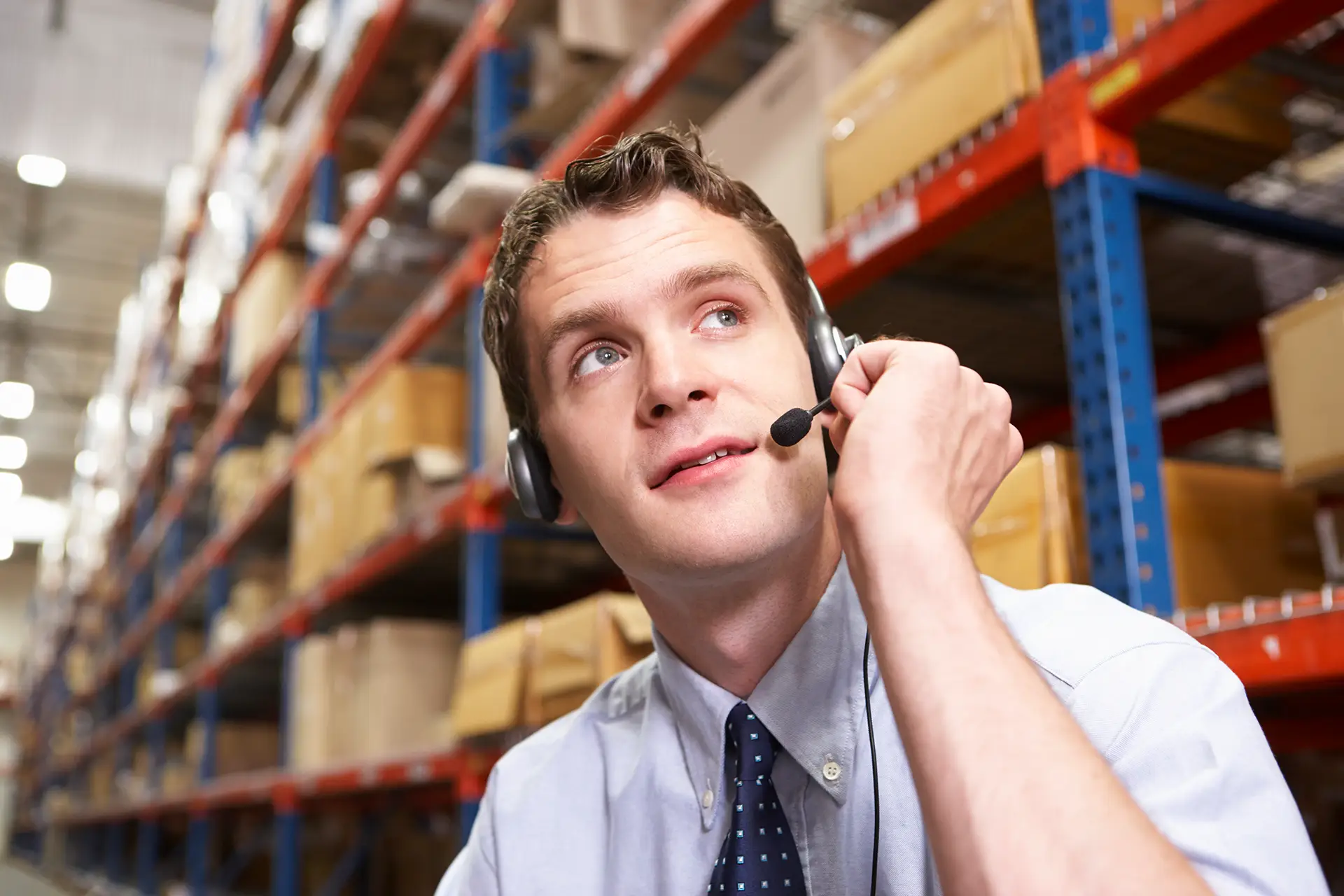 Ein Mann mit Headset sitzt in einer Großen Lagerhalle.